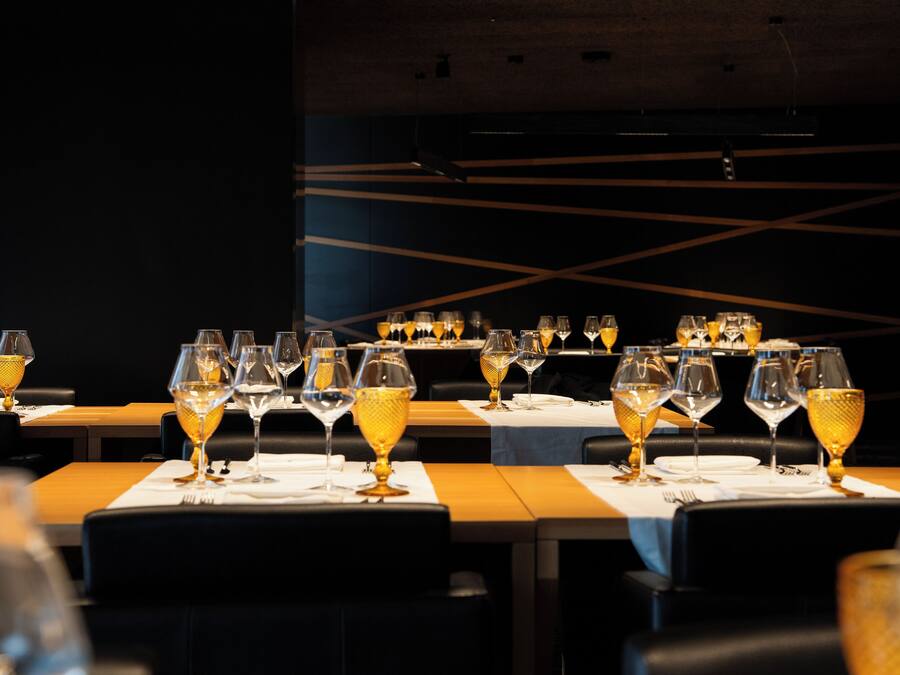 A restaurant with multiple tables set with wine glasses and plates, featuring a modern interior design with dark walls and geometric patterns.