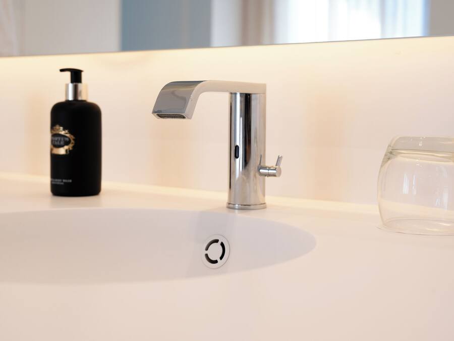 A modern bathroom with a white sink, a black bottle, and a clear glass.