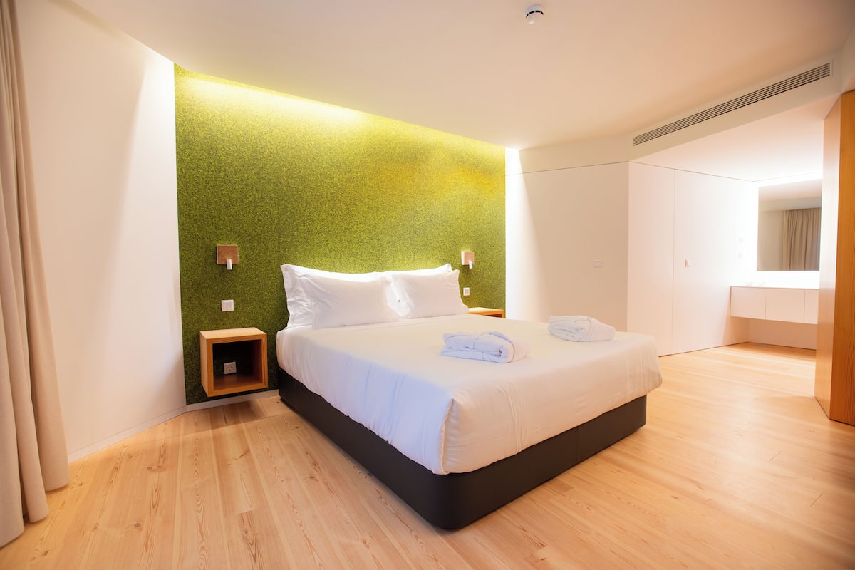 Una habitación de hotel moderna con una cama grande, suelo de madera, pared de acento verde y un armario empotrado.