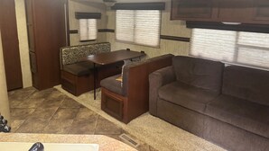 A compact RV interior with a sofa, a small table, and a bench. - Your Peaceful Waterfront Getaway Camping/Fishing Experience with Country Living (Pineview)