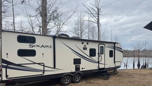 A white RV with "Solaire" branding parked near a body of water. - Your Peaceful Waterfront Getaway Camping/Fishing Experience with Country Living (Pineview)