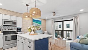 A modern kitchen with white cabinets, a built-in oven, and a microwave. There is a dining area with a blue sofa and a round coffee table. - Private Beach + Chair Service/Pool/Bikes (Santa Rosa Beach)