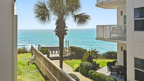 A balcony with a view of the ocean, a palm tree, and a patio area with outdoor furniture. - Private Beach + Chair Service/Pool/Bikes (Santa Rosa Beach)