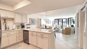 A modern kitchen with white cabinetry, a dishwasher, and a dining area with a sofa and chairs. - Ground Floor Condo with Shared Pool, Golf Access, Bay Views, and WiFi (Panama City)