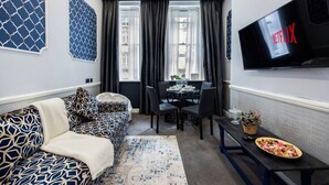A modern living room with a sofa, a dining table, and a TV mounted on the wall. - Stunning Super king & Double Bed Apartment|Central London|Oxford St|Bond St (London)