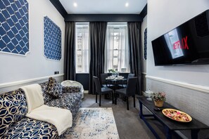 A modern living room with a sofa, a dining table, and a TV mounted on the wall. - Stunning Super king & Double Bed Apartment|Central London|Oxford St|Bond St (London)