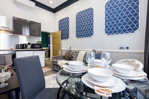 A modern kitchen with built-in appliances, a dining area with a glass table set for a meal, and patterned wall decorations. - Stunning Super king & Double Bed Apartment|Central London|Oxford St|Bond St (London)
