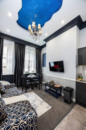 A modern living room with a dining area, a TV mounted on the wall, and a chandelier. - Stunning Super king & Double Bed Apartment|Central London|Oxford St|Bond St (London)