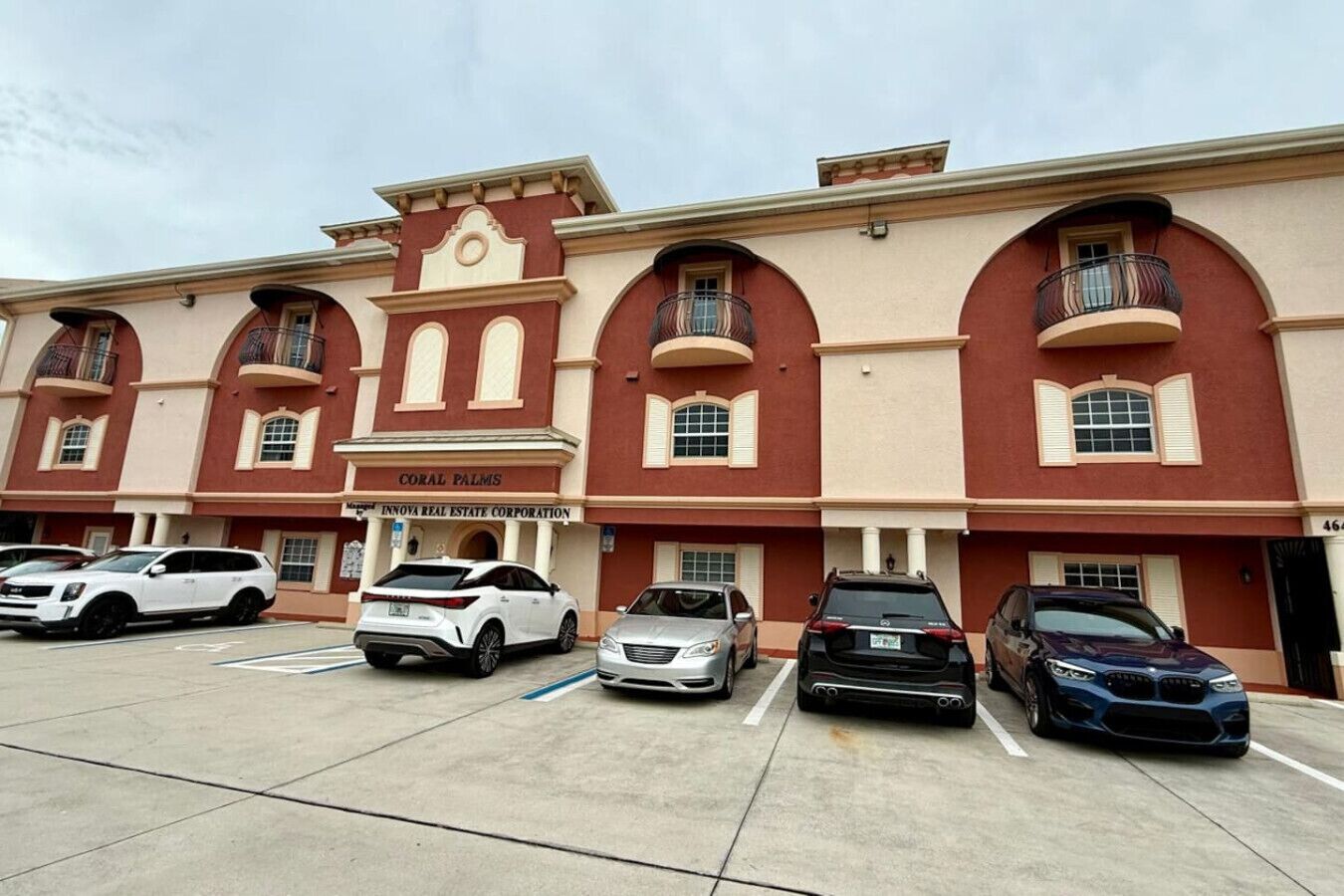 A multi-story building with a red and beige facade, featuring balconies and a sign for 'CORAL PALMS'.