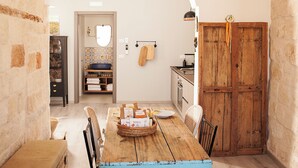 A dining area with a wooden table and chairs, a wicker pendant light, and a view into the kitchen through an archway. - Casa Katha by Monholiday (Monopoli)