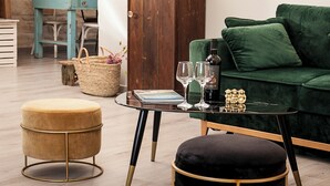 A living room with a green sofa, a wooden cabinet, a round table with wine glasses, and a small stool. - Casa Katha by Monholiday (Monopoli)