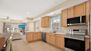 A modern kitchen with wooden cabinets, stainless steel appliances, and a large window with a view. - Oceanside Condo Steps from the Beach and Boardwalk (Ocean City)