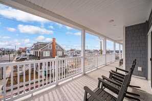 Une véranda couverte donnant sur une rue et des maisons, avec des bancs en bois et une clôture blanche.