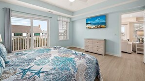 A bedroom with a bed, a dresser, a ceiling fan, a painting, and a view of the outside. - Oceanside Condo Steps from the Beach and Boardwalk (Ocean City)