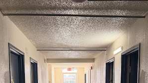 A hallway with a patterned carpet, doors on both sides, and an exit sign at the end. - Wichita's Sunrise inn & Suites (Wichita)