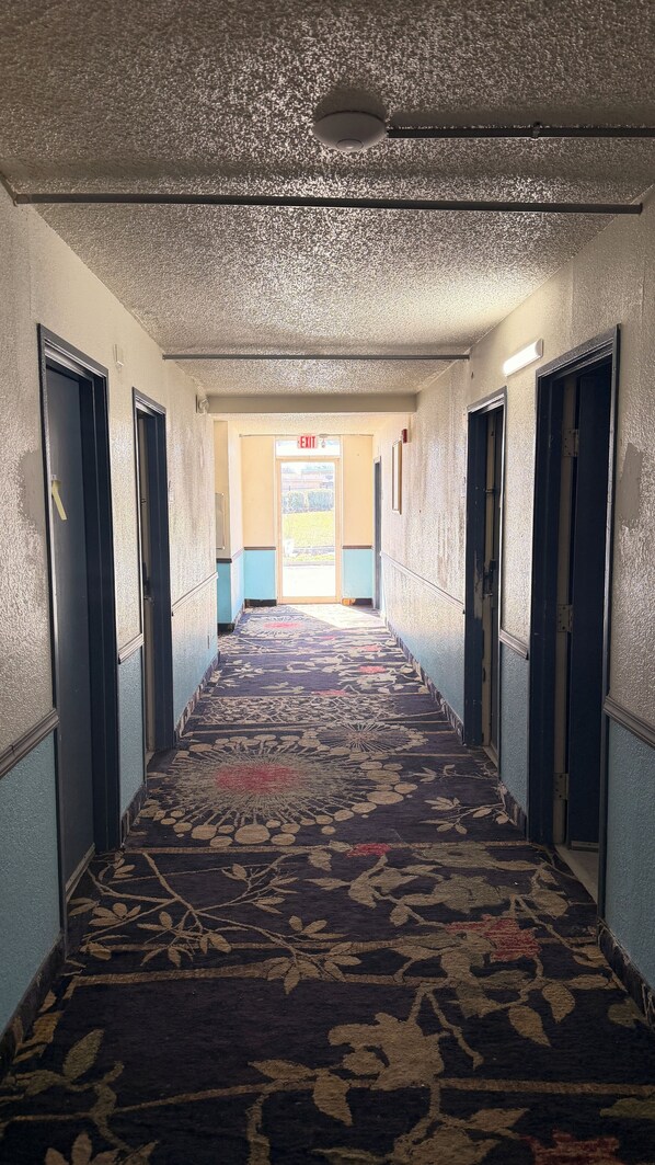 A hallway with a patterned carpet, doors on both sides, and an exit sign at the end.