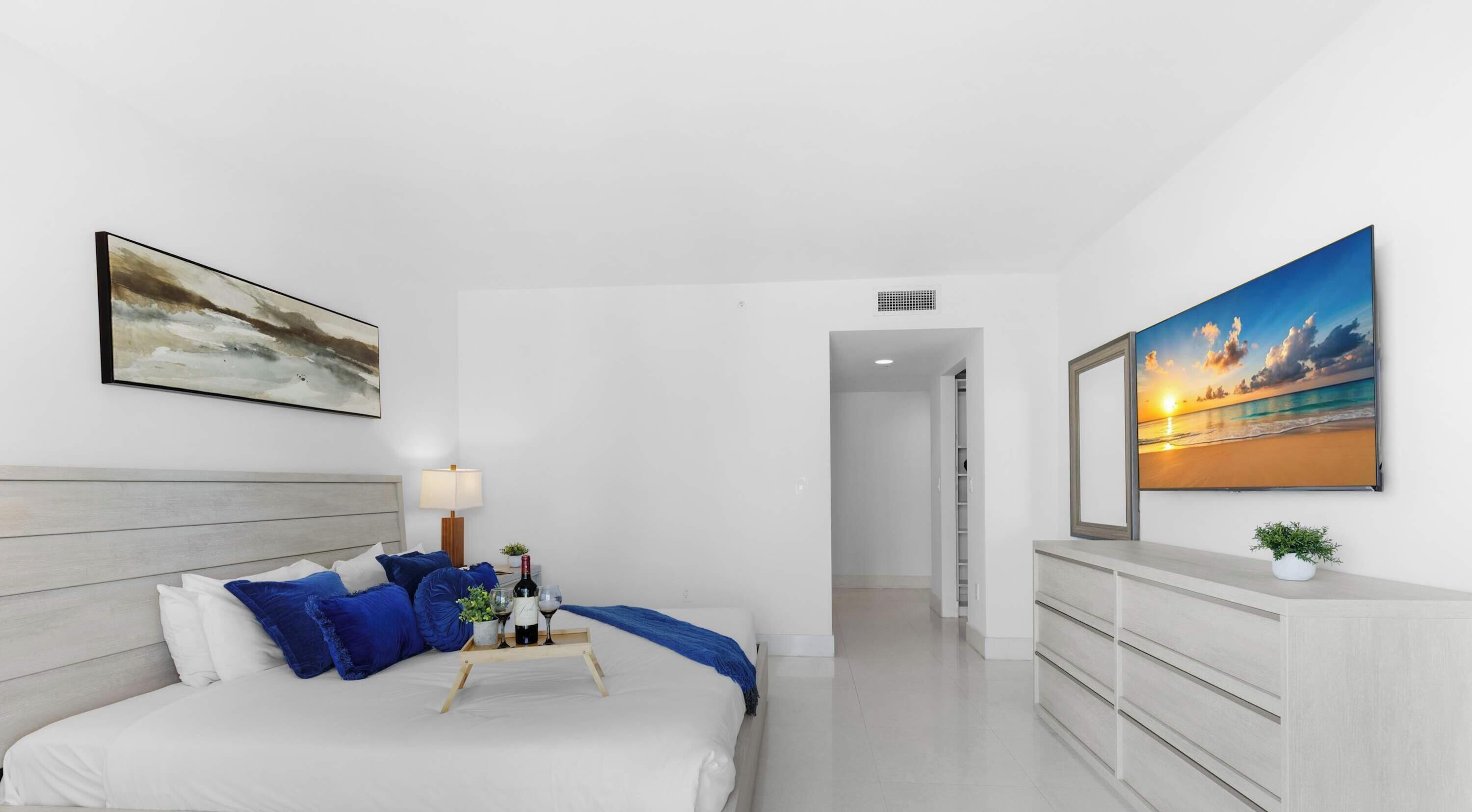 A modern hotel room with a bed, a nightstand, a lamp, a dresser, and two large paintings.