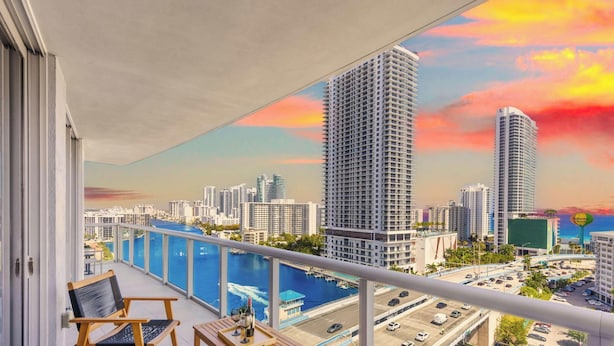 Ein Balkon mit Blick auf eine Stadtlandschaft, einen Swimmingpool und einen Sonnenuntergang.