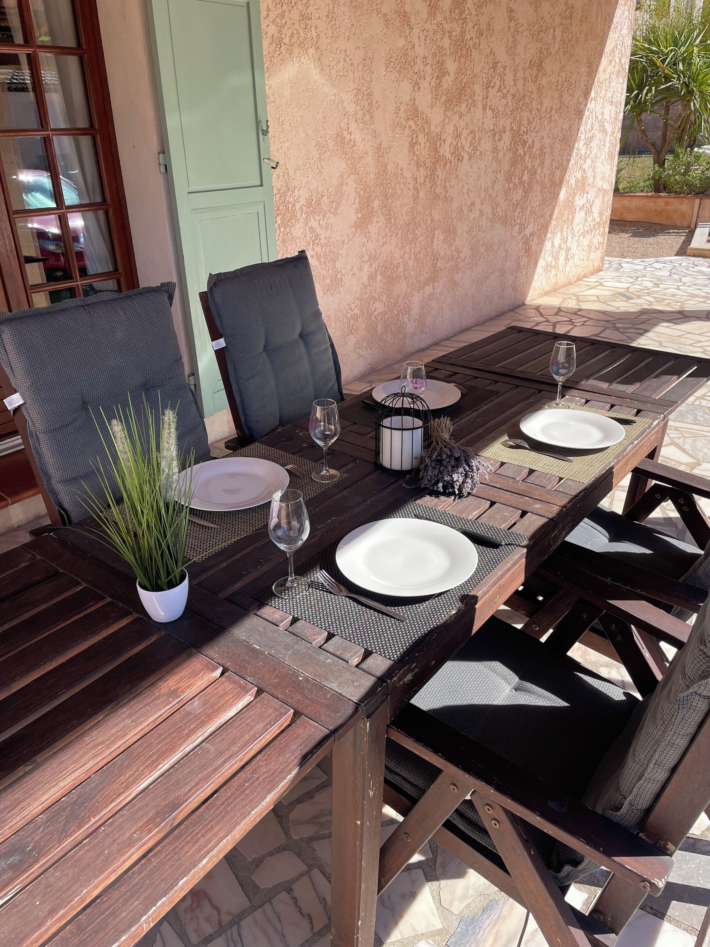 An outdoor dining area with wooden tables and chairs, a potted plant, and a glass of water.