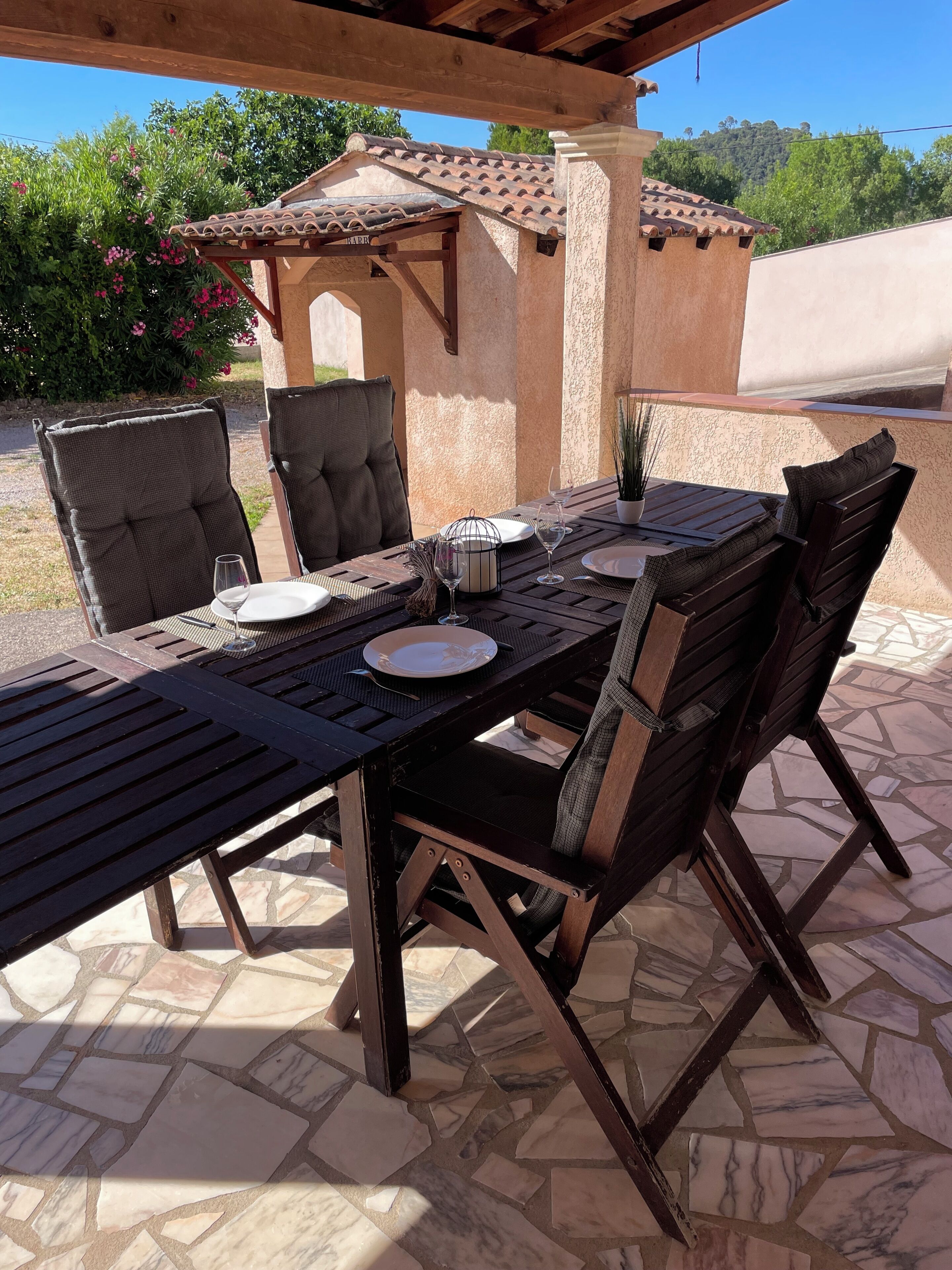 Un patio al aire libre con una mesa lista para comer, rodeada de sillas y una pérgola encima.