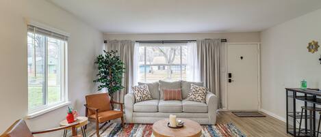 A living room with a beige sofa, a wooden coffee table, a striped rug, and a window with curtains.