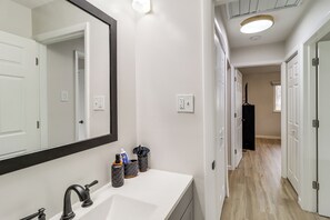 A bathroom with a white sink, a large mirror, and a black faucet. There are two trash bins on the counter. - Cozy 2BR/1BA Ranch - Near Downtown Royal Oak (Oak Park)