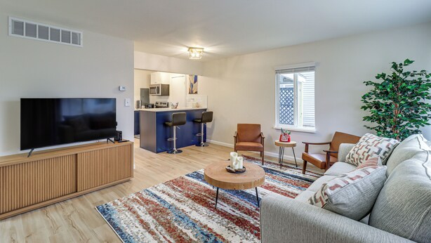 A living room with a TV, sofa, coffee table, and a kitchen area in the background. - Cozy 2BR/1BA Ranch - Near Downtown Royal Oak (Oak Park)