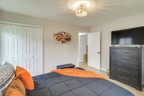 A bedroom with a bed, a dresser, a television, and a door leading to another room. - Cozy 2BR/1BA Ranch - Near Downtown Royal Oak (Oak Park)