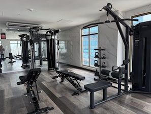 Ein modernes Fitnessstudio mit unterschiedlichen Trainingsgeräten, großen Fenstern und einer Marmorwand.