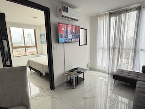 Ein modernes Hotelzimmer mit Bett, einer Couch, einem an der Wand montierten Fernseher und Blick auf die Stadt durch große Fenster.
