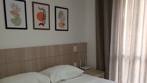 Ein Hotelzimmer mit einem Bett, zwei Kissen, einem Nachttisch mit Lampe und drei gerahmten Kunstwerken an der Wand.
