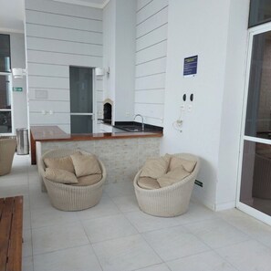 A modern kitchen with a built-in oven, a sink, and a wooden countertop. There are two wicker chairs with cushions and a wooden table. - METROPOLITAN/BARCELONA/REFINEMENT (Goiânia)