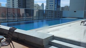 Ein Pool auf dem Dach mit klarem, blauem Wasser, umgeben von einer Glasbrüstung. Treppen führen zum Pool hinab, und einige Liegestühle sind sichtbar.