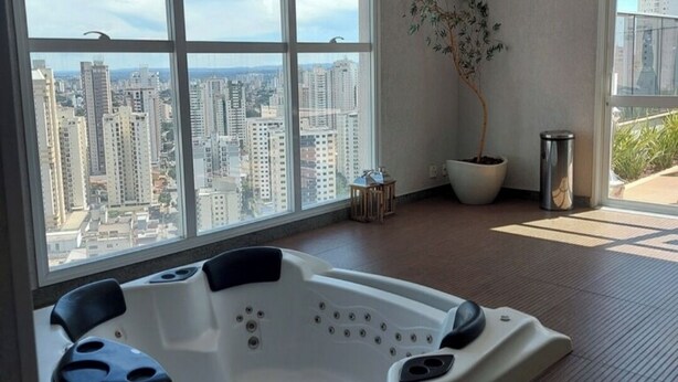 Ein modernes Badezimmer mit einer großen Badewanne, einem Blumentopf und Blick auf eine Stadtkulisse durch große Fenster.