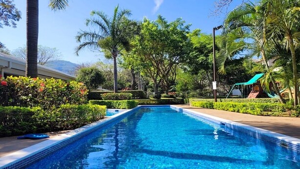 A rectangular swimming pool with clear blue water, surrounded by lush greenery and palm trees. - Near Airport, Lush Gardens, Pool, King Bed, Security SANTA ANA NEAR DOWNTOWN (Santa Ana)