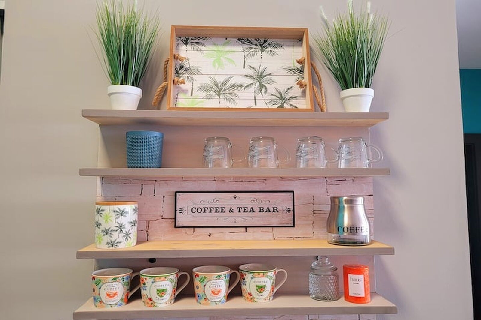 A coffee and tea bar with shelves displaying mugs, a coffee pot, and a sign.
