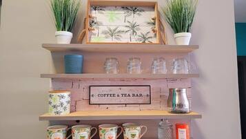 A coffee and tea bar with shelves displaying mugs, a coffee pot, and a sign.