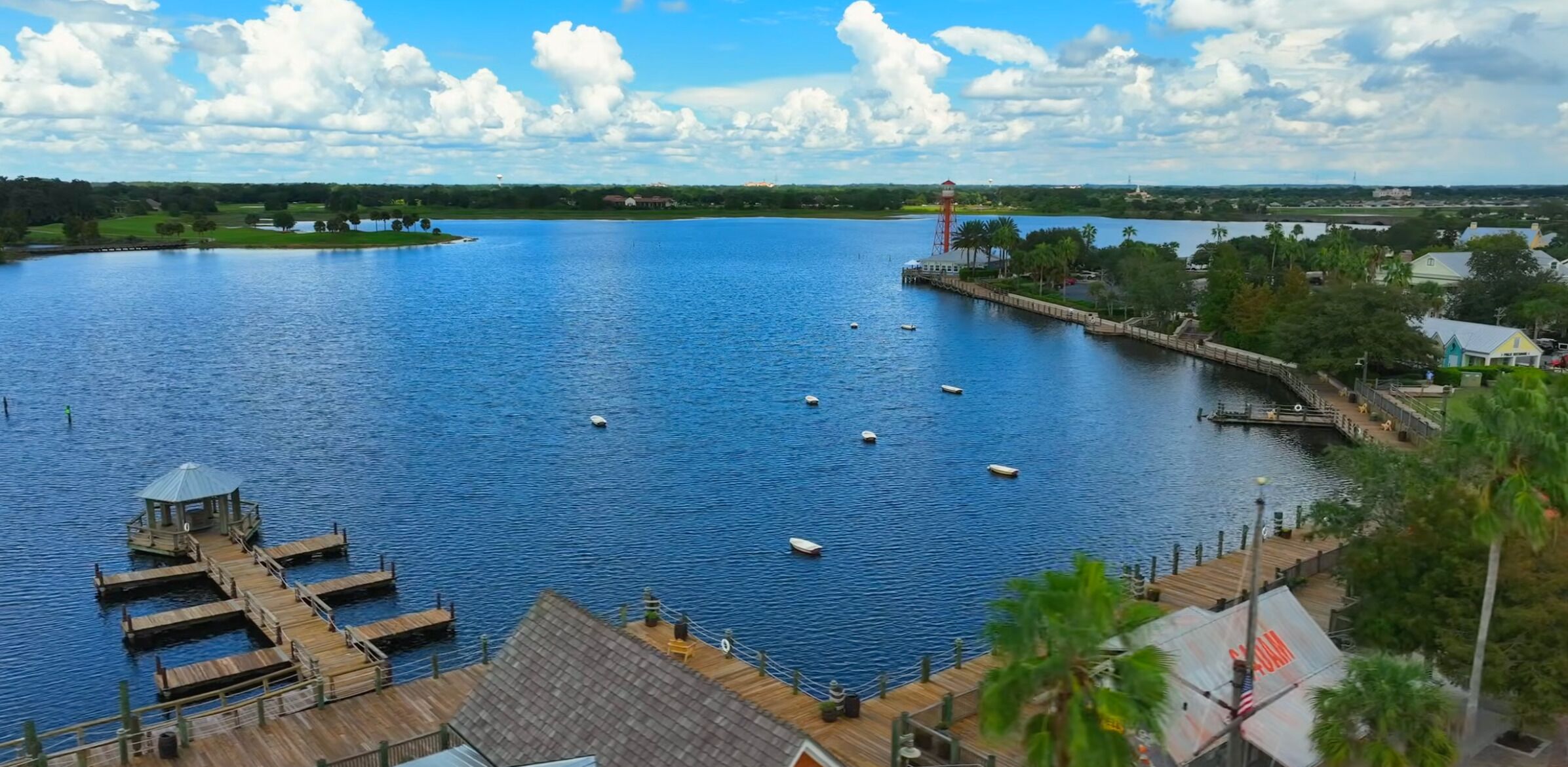 A waterfront view with a dock, boats, and a lighthouse.