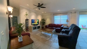 A living room with a television, a ceiling fan, a red couch, a black sofa, and a coffee table. - Pet friendly Charming Bonnybrook Villa! (The Villages)