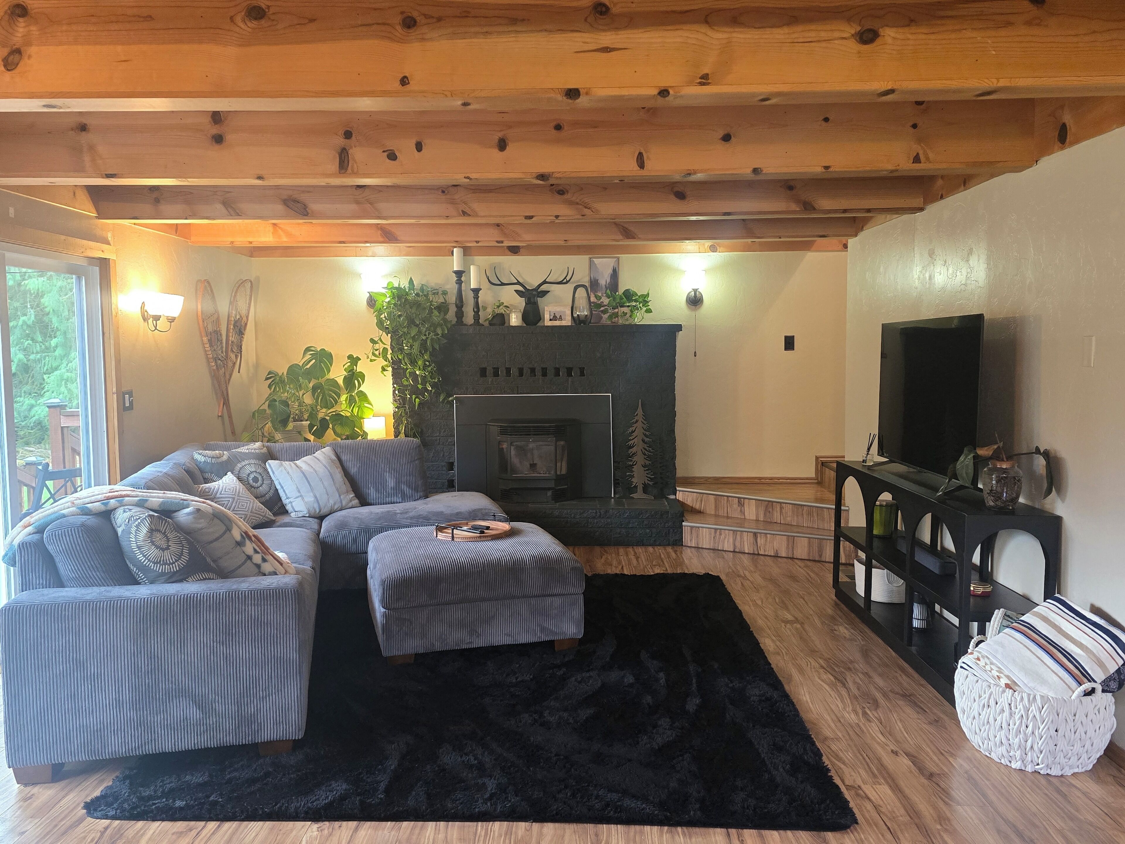 A cozy living room with a fireplace, a sectional sofa, a black rug, and a television.