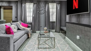 Een moderne woonkamer met een bank, een glazen salontafel, een wandklok en een televisiescherm waarop het Netflix-logo te zien is.
