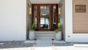 A modern entrance with a wooden door, potted plants, and a concrete pathway leading to a patio area. - Luxury Beachfront Mansion (Provincia de Guanacaste)