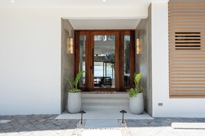 A modern entrance with a wooden door, potted plants, and a concrete pathway leading to a patio area. - Luxury Beachfront Mansion (Provincia de Guanacaste)