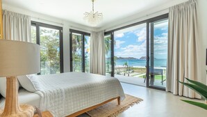 A bedroom with a large bed, a bedside lamp, and a view of the ocean through floor-to-ceiling windows. - Luxury Beachfront Mansion (Provincia de Guanacaste)