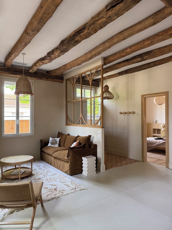 A room with exposed wooden beams, a sofa with cushions, a woven table, and a patterned rug. - Stunning Villa in the Arcachon Basin with a Pool (Audenge)
