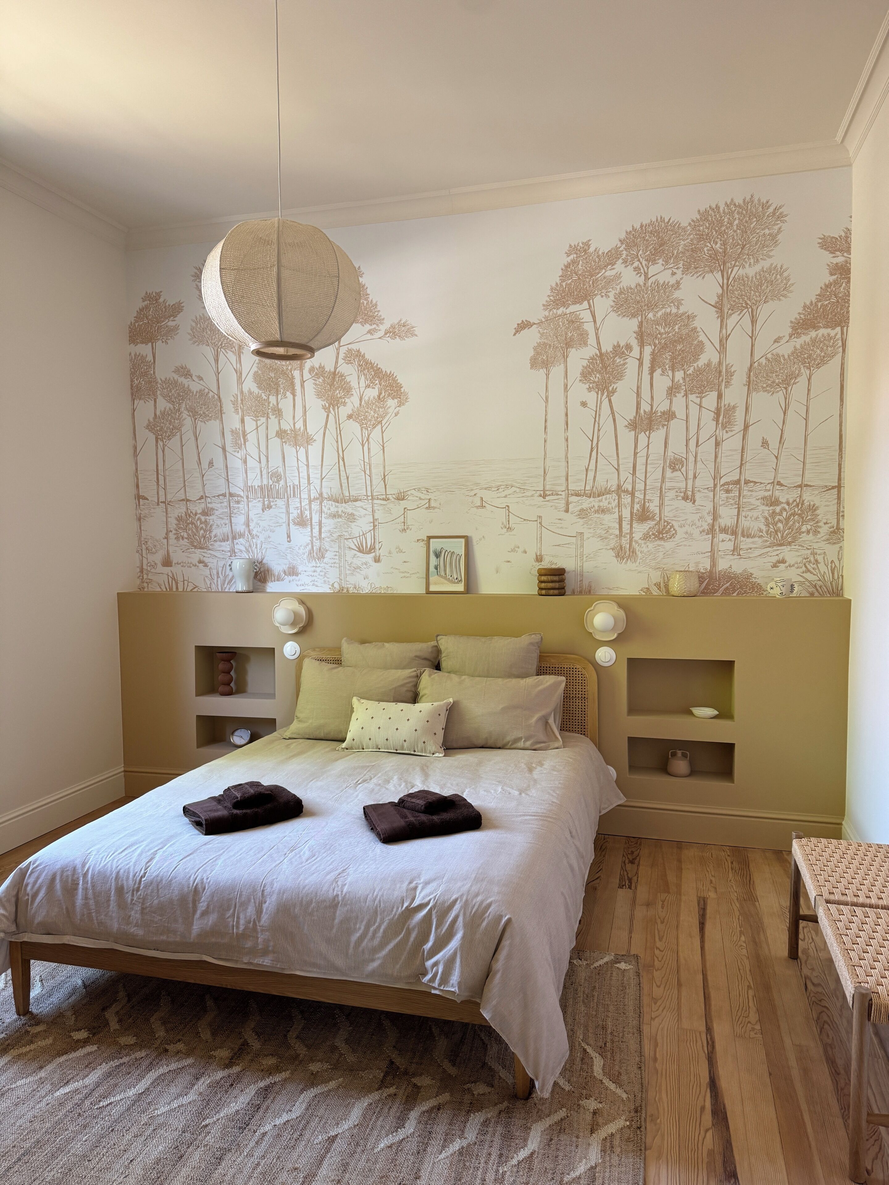 Une chambre à coucher comprenant un lit, une étagère fixée au mur, une table de chevet et un luminaire suspendu.
