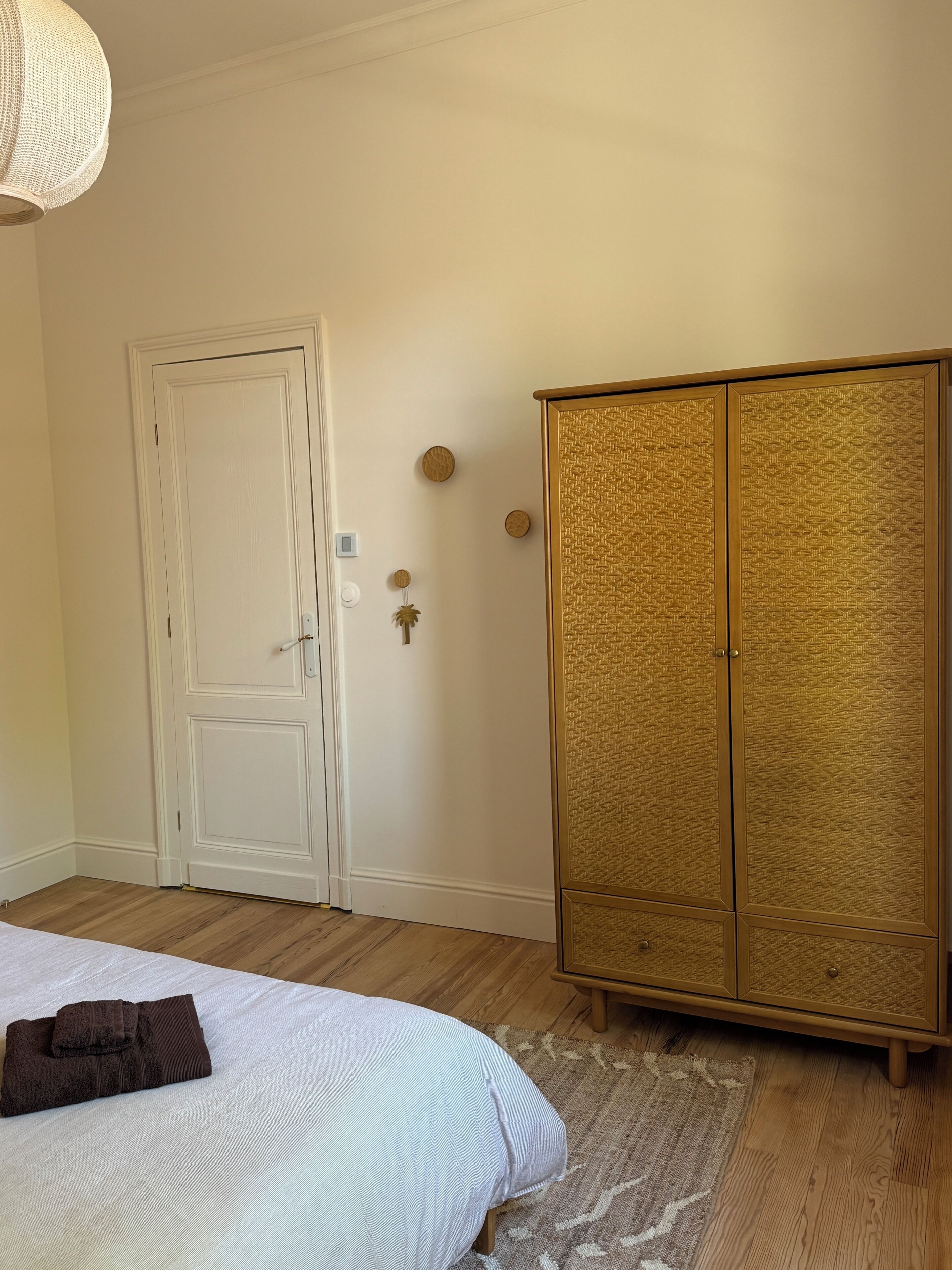 Un dormitorio con cama, armario, una puerta y una lámpara fijada a la pared.