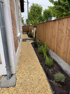 A narrow pathway with gravel, bordered by a wooden fence and a brick wall. - Stunning Villa in the Arcachon Basin with a Pool (Audenge)
