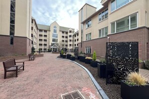 A courtyard with brick pathways, benches, planters, and a decorative metal fence. - Songhees Sunrise (Victoria)