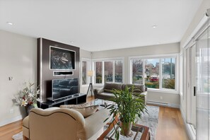 A modern living room with a flat-screen TV, comfortable seating, a large window, and a view of the outside. - Songhees Sunrise (Victoria)